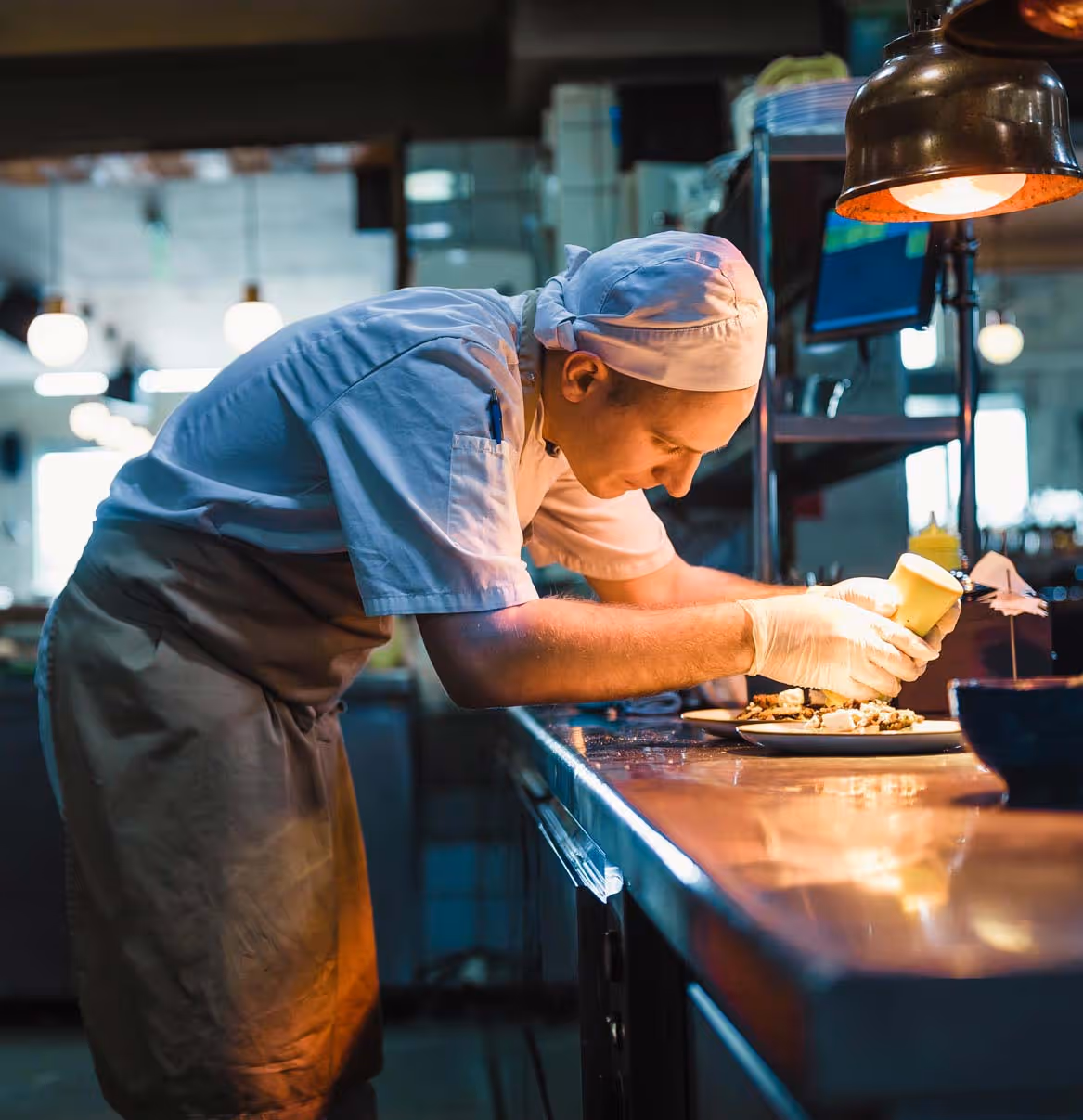 Chef plating dishes under a heat lamp in a commercial kitchen